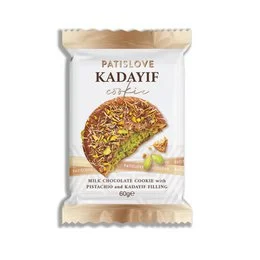 Milk chocolate cookie with a pistachio and kadayif filling. The cookie has a round, flat shape and a golden-brown color. The filling is visible through the transparent packaging, showing the pistachio and kadayif pieces inside.