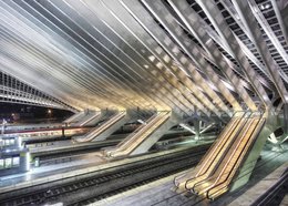 This image depicts an architectural interior with a complex, geometric design featuring escalators and a futuristic, abstract aesthetic. The image showcases a striking, modern design with intersecting lines, angles, and patterns that create a visually striking and dynamic composition.
