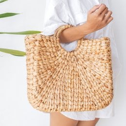 Woven straw shopping bag made of water hyacinth, featuring a round, basket-like shape and a large open compartment for carrying items.