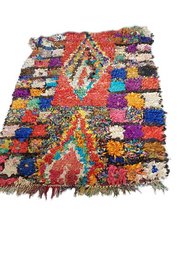 Colorful, patterned Boucherouite runner rug with a mix of vibrant hues and geometric designs. Made of recycled textiles, this unique floor covering features a striking diamond motif and a variety of shapes and textures.