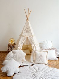 Boho-style teepee tent for kids with frills, embroidery, and a floral design. Includes a cozy floor cushion and decorative accents.