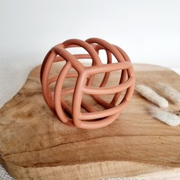 Flexible silicone motor ball rattle in rust color, designed for babies. Unique shape with open lattice design provides visual and tactile stimulation.