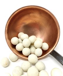 White chocolate-coated coconut and hazelnut candies in a wooden bowl. The candies are round, white, and appear to be made of a creamy, sweet confection.