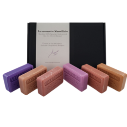 A set of handmade soap bars in various colors and scents, including violette, bois de santal, calendula, argile rouge, cannelle orange, and fleur des iles.