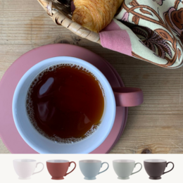 A set of 6 ceramic teacups in various pastel colors including white, terracotta rose, ice, leaf, and almost black. The teacups are displayed alongside a pink mug filled with a hot beverage.