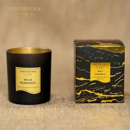 A black glass candle with a gold label that reads "Wild Romance" and features a burning flame. The candle is presented in a black and gold box.