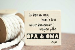 A white card with handwritten text in Dutch that reads "It may be a little weird, but I'm so proud of you" and "Opa & Oma" (Grandpa & Grandma). The card is placed on a wooden surface with a coiled rope.