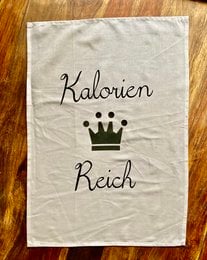 A white kitchen towel with the text "Kalorien Reich" (Calorie Kingdom) printed in black, featuring a crown icon. The towel appears to be made of cotton or a similar natural fabric material.