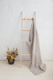  Cozy, diamond-patterned Aran blanket in oat color, made of soft, warm material, perfect for snuggling up on the couch or bed.