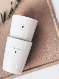 A set of two white porcelain mugs with various text and heart designs, including "Wow Mom", "Daddy Cool", "Morgähn", "Buongiorno", "Ciao Bella", "Best Wishes", "Hey You", and "Favorite". The mugs are displayed on a wooden surface with some leaves.