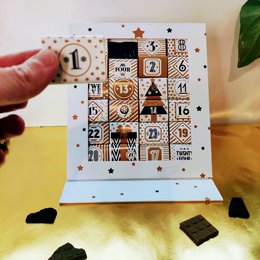 Advent calendar with 24 chocolate-filled compartments, featuring festive designs including a Christmas tree, stars, and other holiday motifs.