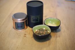 Osthmantus flower and ginger scented candle with a round, tall shape. The candle is presented in a black container with a silver lid.