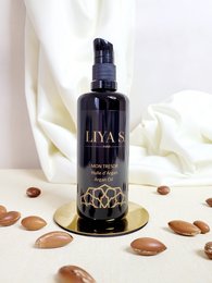 Organic argan oil cream in a dark glass bottle with a gold floral design. The product is suitable for skin care and moisturizing.