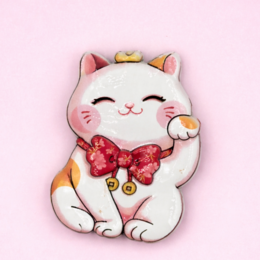 A white ceramic cat figurine with a red bow and paw-shaped magnets. The cat has a happy, smiling expression.