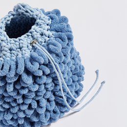 "Maya" bucket bag in light blue, burgundy + black, and beige + blue colors. Made of soft, textured material with a drawstring closure and shoulder strap.