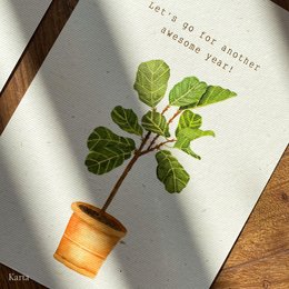 A birthday postcard featuring a potted ficus plant with green leaves. The text on the card reads "Let's go for another adventure year!"