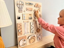 Beige wooden busy board with various shapes, textures, and sensory elements for toddlers to explore and develop fine motor skills.