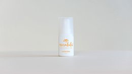 A white and orange eye cream container with a pump dispenser, sitting on a wooden surface with a towel and other natural elements.