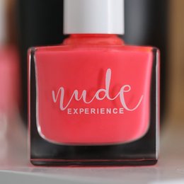 Bright pink nail polish with the text "Nude Experience" on the bottle. The nail polish is being held in a hand, showing a vibrant, glossy pink manicure.
