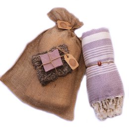  "A set of bath and body products in a burlap bag, including a purple and white striped towel or blanket. The products appear to be a gift set for relaxation or self-care."