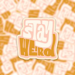 Vinyl sticker with the text "Stay Weird" in a stylized font against a patterned background.