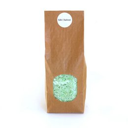 A green, textured sensory toy made of rice, packaged in a brown paper bag.