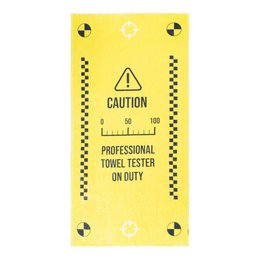 A large yellow beach towel with the text "PROFESSIONAL TOWEL TESTER ON DUTY" printed on it. The towel has a caution sign and checkered pattern design.