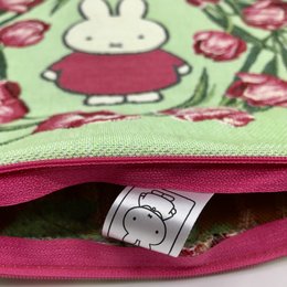 A green pillow with a Miffy character and red tulips printed on it. The pillow has a pink zipper and a Miffy logo tag visible.