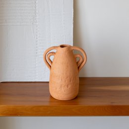  Handmade ceramic pottery vase in a warm orange-brown color with two handles. The vase has a simple, minimalist design and appears to be made of high-quality materials.