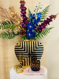 Tall, decorative vase with vibrant blue and purple flowers, ferns, and geometric patterns.