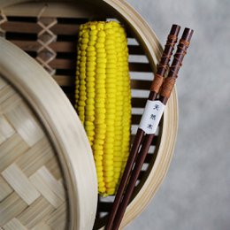 Yellow corn cobs, wooden chopsticks, and a wooden box with the label "MATS" on a wooden surface.