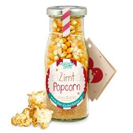 Cinnamon-flavored popcorn in a glass jar, with a festive label. The popcorn appears to be a mix of yellow and white kernels, with a warm, spiced aroma.