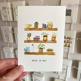 Colorful greeting card featuring a bookshelf with various potted plants, books, and decorative items. The text "Dank je wel" (Dutch for "Thank you") is written at the bottom.