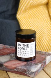 A tall, round, cedarwood and fir needle scented candle in a simple black glass container with a white label that reads "IN THE FOREST".