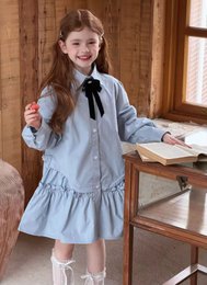  Light blue kids shirt dress with black bow collar, long sleeves, tiered ruffle skirt, classic preppy style.