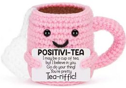  A pink crocheted mug with the text "POSITIVI-TEA" and a friendly, smiling face. The mug appears to be a tea-themed push or pull toy.