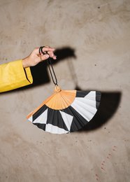 Handmade Spanish fan with geometric black, white, and orange pattern. Decorative accessory.