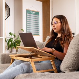 Nomada Tilting Laptop Tray - Adjustable wooden laptop stand with tilting surface for comfortable use on a couch or bed.