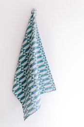 "Teal and white patterned tea towel with a rustic wooden board, sliced bread, and small bowls of olives and corn."