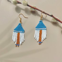  Handmade, statement earrings in a vibrant red, white, and blue color palette. The earrings feature a triangular shape with beaded fringe detailing, creating a bold and eye-catching accessory.