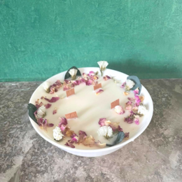 A round, tall, rose-scented candle with a floral design on the surface.