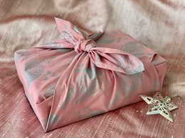  A set of 3 pink furoshiki wrapping cloths with a floral pattern. The furoshiki are folded and tied in a knot, creating a decorative wrapping for gifts or other items.