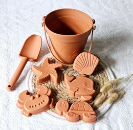 Rust-colored silicone bucket with assorted bath toy molds, including shapes like hearts, animals, and other designs. Suitable for kids' bath time.