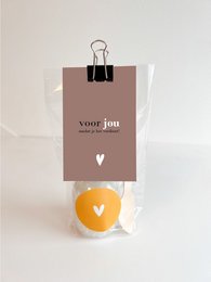 Gift bag containing bath salts in a neutral-colored package with a yellow accent. Includes a wooden spoon for scooping.