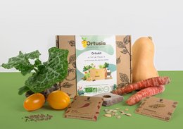 A box containing various gardening supplies, including a packet of seeds, a gardening tool, and some vegetables. The box is made of cardboard and has a natural, earthy appearance.