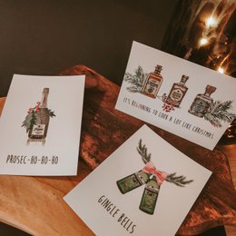 Set of 9 Christmas cards featuring festive alcohol-themed designs with text and illustrations of bottles, glasses, and holiday decorations.