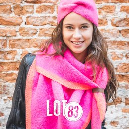 A bright pink scarf with the text "Love 83" printed on it. The scarf is worn by a smiling woman with long brown hair, who is also wearing a beige coat and a pink hat.