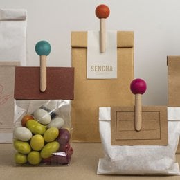 Wooden bag clip in various colors including orange, rose, bordeaux, vert anis, bleu canard, and bleu nuit. Clip features a round wooden handle.