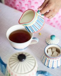 Ceramic milk pot with blue striped pattern, red rim, turquoise handle, round shape, colorful masquerade design.