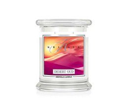  A medium-sized scented candle in a glass jar, featuring a warm, desert-inspired fragrance of oud wood and spices. The candle has a vibrant, gradient-style label in shades of red, orange, and pink, evoking a desert landscape.